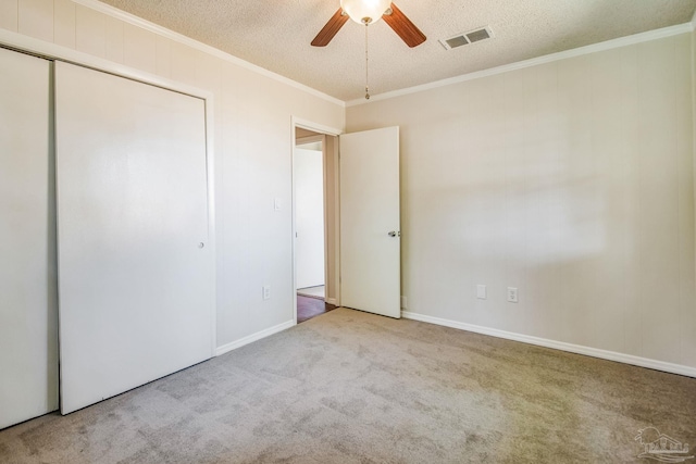 unfurnished bedroom featuring crown molding, a textured ceiling, ceiling fan, a closet, and light colored carpet