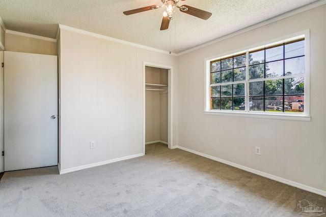 unfurnished bedroom featuring ceiling fan, ornamental molding, a textured ceiling, light colored carpet, and a closet