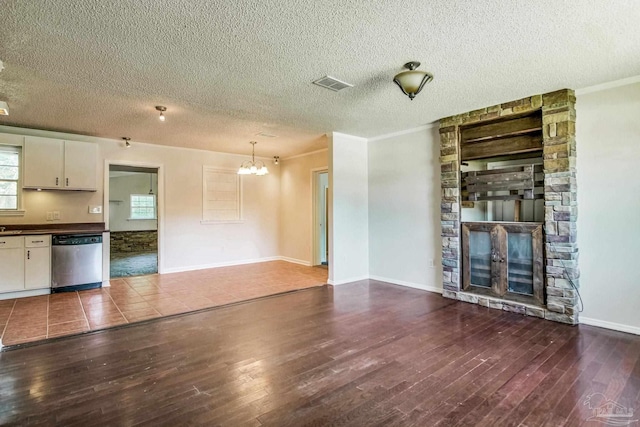 unfurnished living room featuring crown molding, an inviting chandelier, dark hardwood / wood-style floors, a fireplace, and a textured ceiling