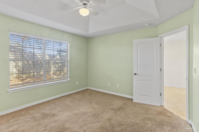 empty room with light carpet, ceiling fan, and a raised ceiling