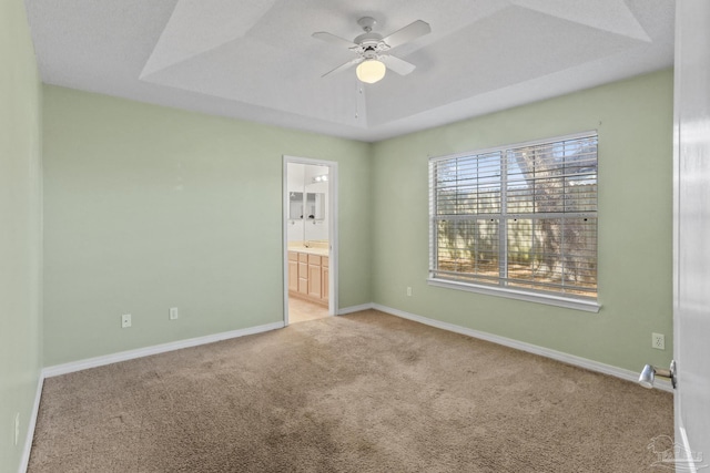 unfurnished bedroom with ceiling fan, ensuite bath, a raised ceiling, and light carpet