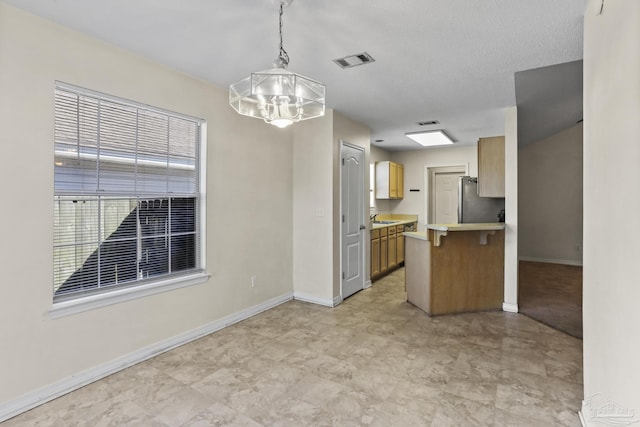 kitchen featuring kitchen peninsula, stainless steel fridge, a notable chandelier, and decorative light fixtures