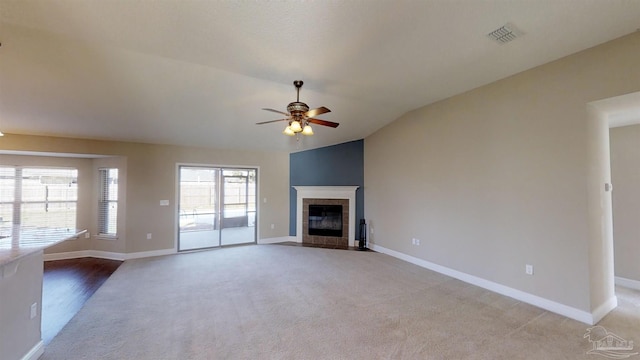 unfurnished living room featuring a tiled fireplace, lofted ceiling, light carpet, and ceiling fan