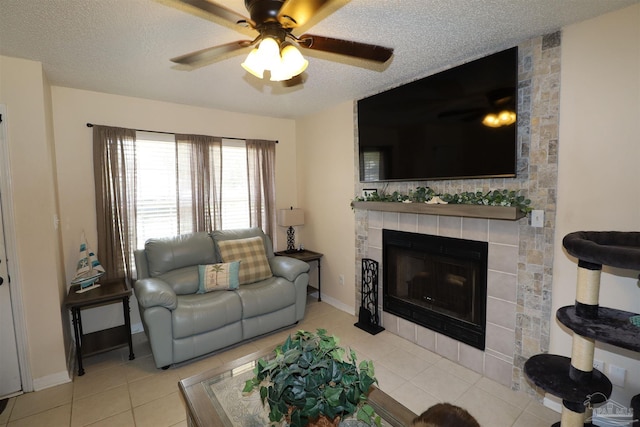 living room featuring ceiling fan, a fireplace, a textured ceiling, and light tile patterned floors