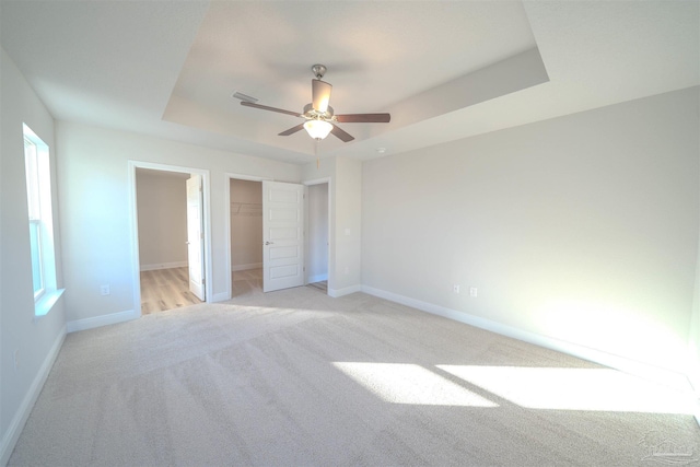 unfurnished bedroom featuring ceiling fan, a tray ceiling, light carpet, a spacious closet, and a closet