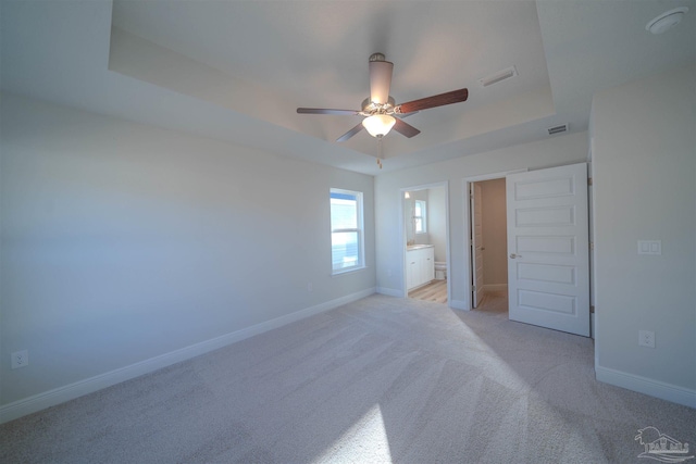 unfurnished bedroom featuring ceiling fan, ensuite bath, a raised ceiling, and light carpet