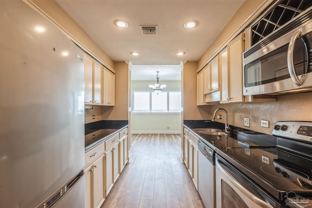 kitchen featuring sink, light wood-type flooring, appliances with stainless steel finishes, a chandelier, and cream cabinetry