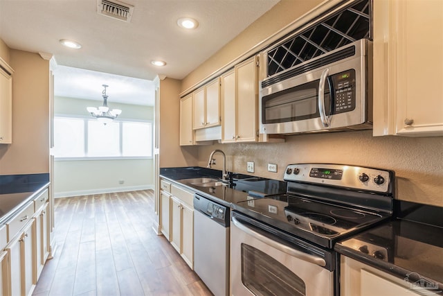 kitchen featuring stainless steel appliances, light hardwood / wood-style floors, an inviting chandelier, sink, and cream cabinetry