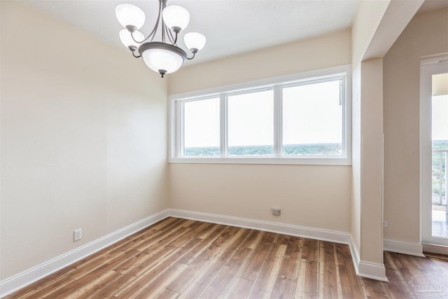 empty room with a wealth of natural light, wood-type flooring, and a chandelier