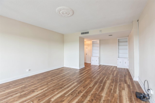 unfurnished room with built in features, a textured ceiling, and wood-type flooring