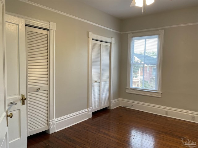 unfurnished bedroom with dark hardwood / wood-style floors, two closets, and ceiling fan