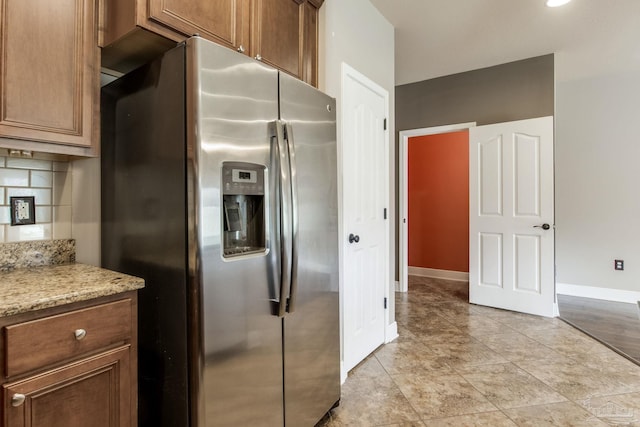 2107 Wilsons Plover Cir, Navarre, FL 32566 - kitchen with stainless steel refrigerator with ice dispenser, baseboards, brown cabinets, and light stone counters