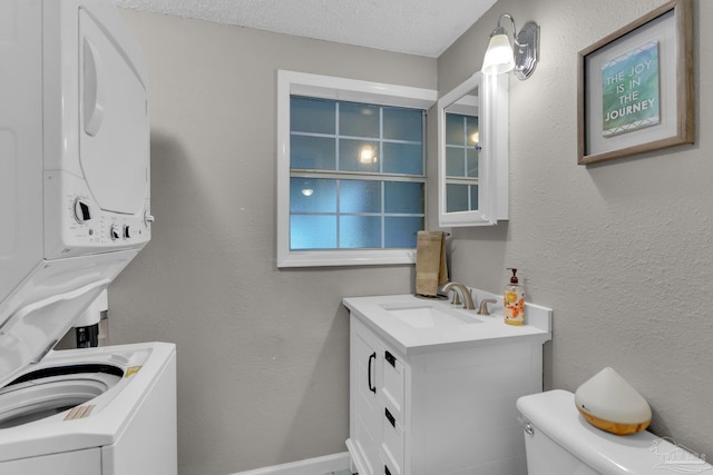 bathroom with stacked washer / drying machine, toilet, a textured ceiling, and vanity