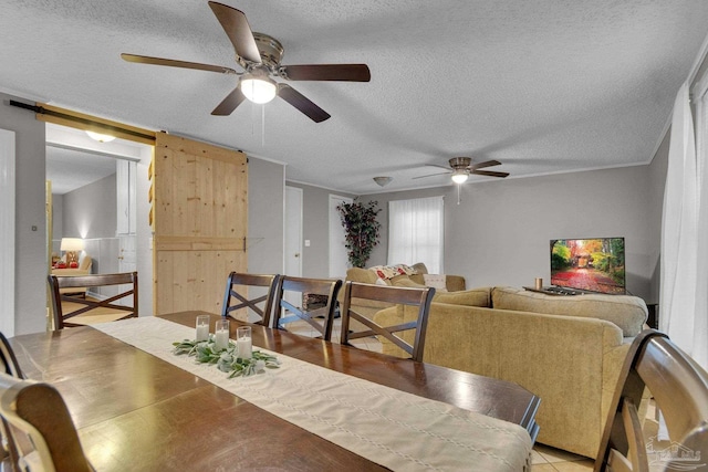 dining space with a textured ceiling, a barn door, ceiling fan, and light tile patterned flooring