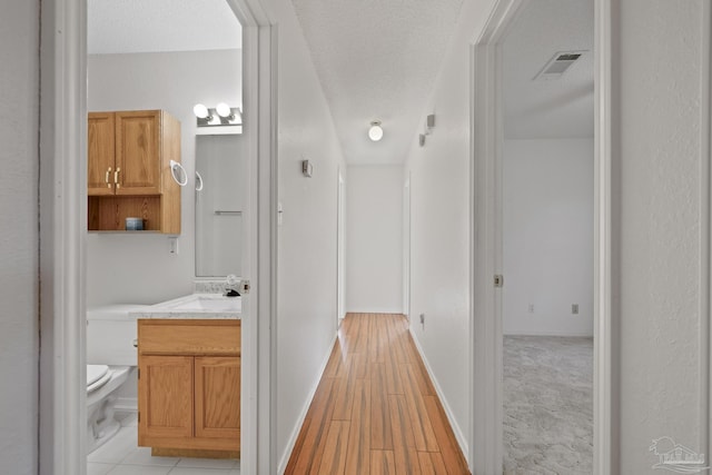 5362 Barbarosa Rd, Gulf Breeze, FL 32563 - corridor with a textured ceiling, visible vents, light wood finished floors, and a sink