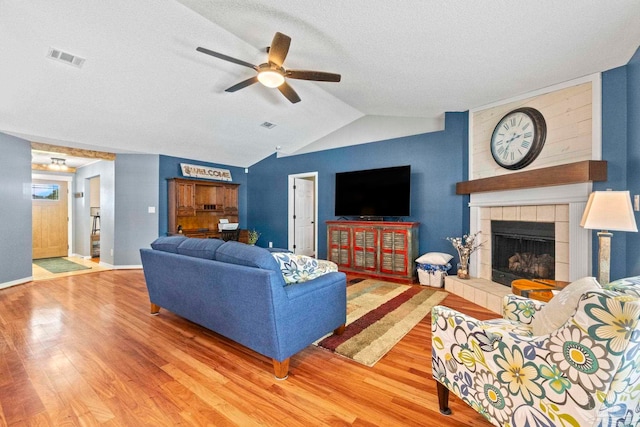 living area with a tiled fireplace, a textured ceiling, ceiling fan, and wood finished floors