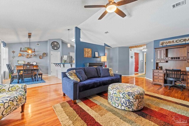 living room with a ceiling fan, a textured ceiling, visible vents, vaulted ceiling, and light wood-style flooring
