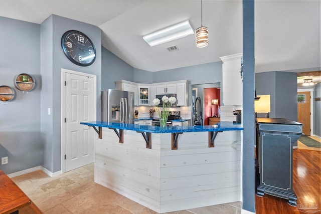 kitchen featuring visible vents, glass insert cabinets, a kitchen bar, white cabinetry, and stainless steel appliances