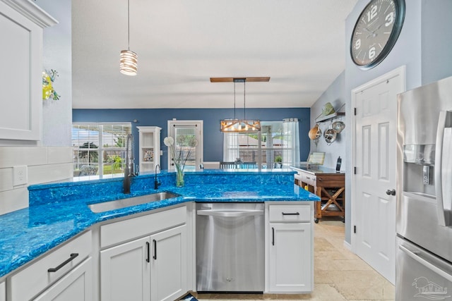 kitchen with decorative light fixtures, a sink, white cabinets, stone tile flooring, and stainless steel appliances