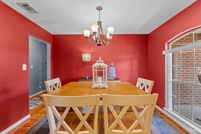 dining room with visible vents, a textured ceiling, wood finished floors, and a chandelier