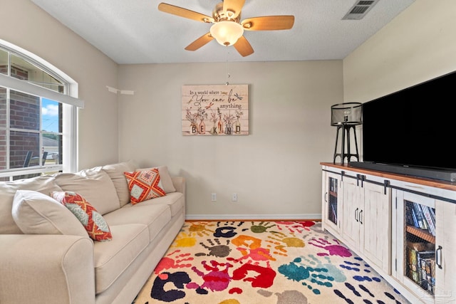 living area with a textured ceiling, ceiling fan, visible vents, and baseboards