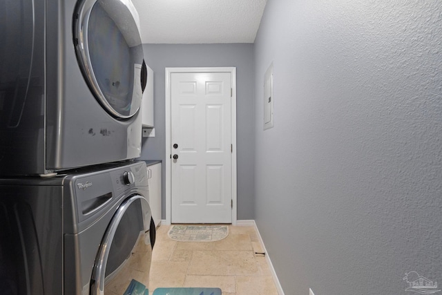 clothes washing area with laundry area, stone tile floors, baseboards, stacked washing maching and dryer, and a textured ceiling