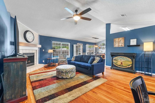 living area featuring ceiling fan, a fireplace, a textured ceiling, and wood finished floors