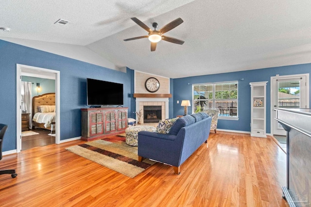 living area with light wood finished floors, a textured ceiling, a ceiling fan, a tile fireplace, and vaulted ceiling