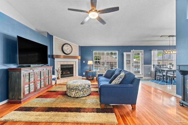 living room featuring a textured ceiling, wood finished floors, a tile fireplace, ceiling fan with notable chandelier, and lofted ceiling