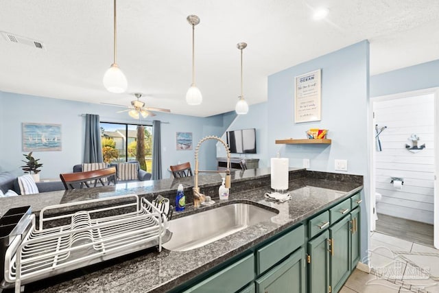 kitchen featuring visible vents, dark stone counters, green cabinetry, decorative light fixtures, and a sink