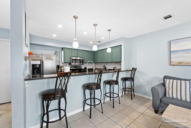 kitchen featuring stainless steel appliances, a breakfast bar, visible vents, and green cabinetry