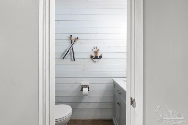 bathroom featuring wood walls, vanity, toilet, and wood finished floors