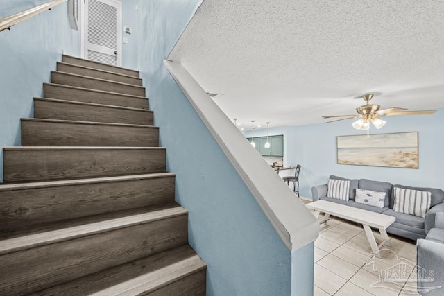 stairs with ceiling fan, a textured ceiling, and tile patterned flooring