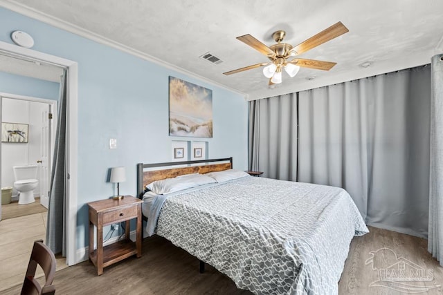 bedroom with visible vents, a ceiling fan, ensuite bath, wood finished floors, and crown molding