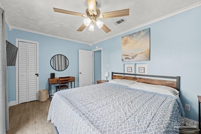 bedroom featuring wood finished floors, a ceiling fan, visible vents, a closet, and crown molding