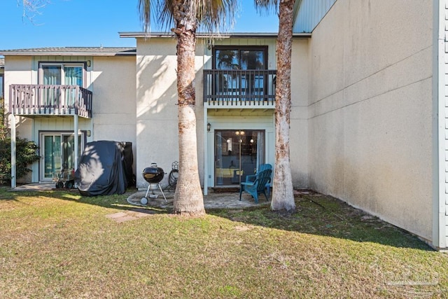 rear view of house featuring a balcony, a lawn, and stucco siding