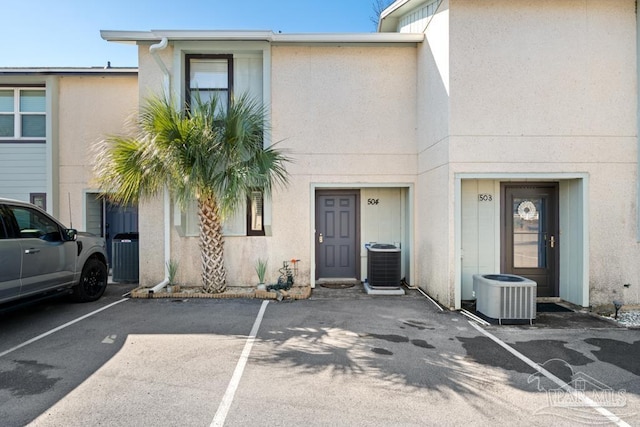 townhome / multi-family property with uncovered parking, cooling unit, and stucco siding