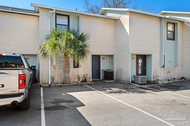 townhome / multi-family property with uncovered parking, central AC unit, and stucco siding