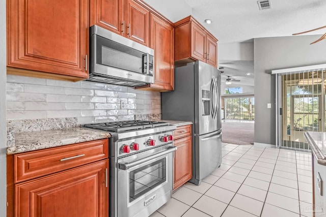 kitchen featuring ceiling fan, tasteful backsplash, light stone counters, light tile patterned flooring, and appliances with stainless steel finishes