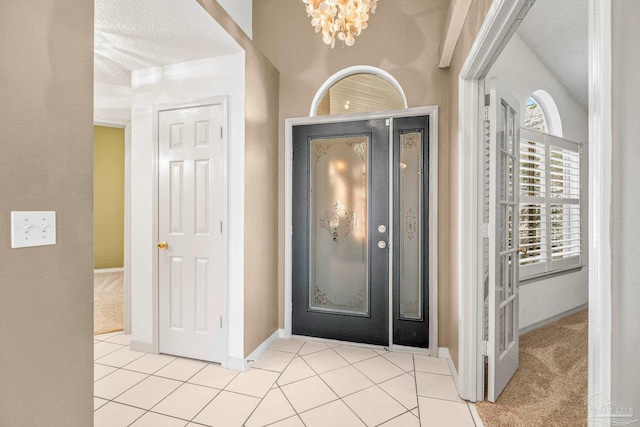 tiled entrance foyer featuring a textured ceiling and a chandelier