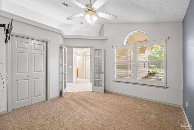 unfurnished bedroom with a textured ceiling, light colored carpet, vaulted ceiling, and ceiling fan