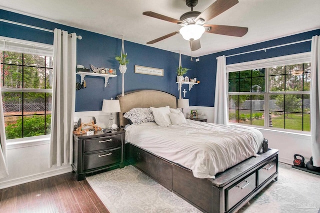 bedroom featuring baseboards, a ceiling fan, wood finished floors, and multiple windows