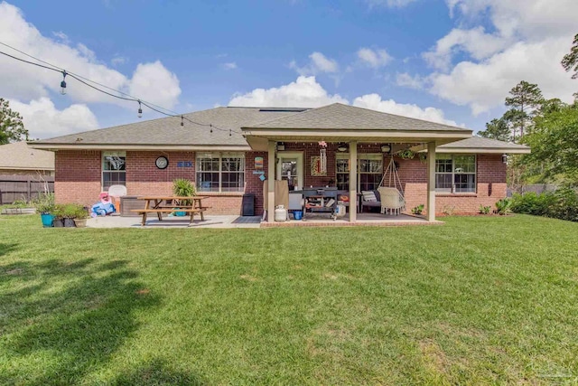 rear view of house featuring a lawn, brick siding, fence, and a patio