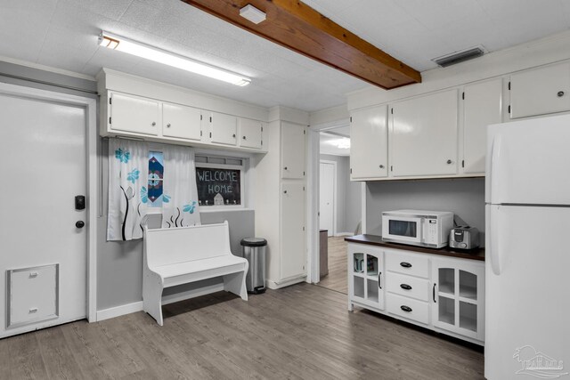 kitchen featuring white appliances, light hardwood / wood-style floors, white cabinetry, and beamed ceiling