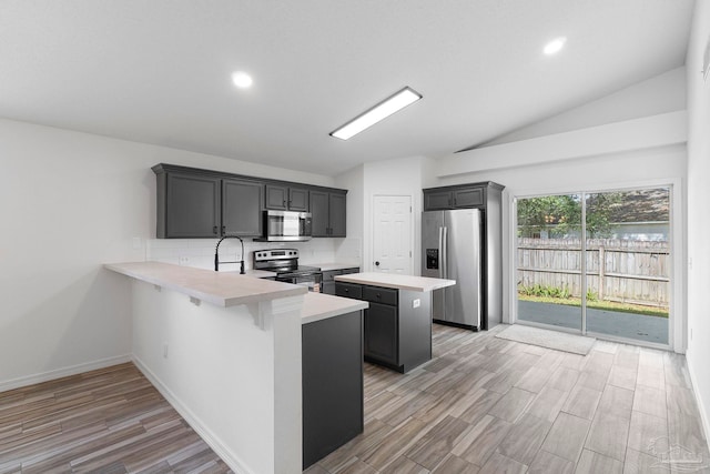 1042 Simpson St, Pensacola, FL 32526 - kitchen with appliances with stainless steel finishes, a kitchen island, light countertops, vaulted ceiling, and light wood-style flooring