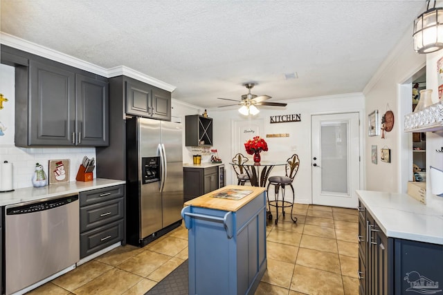 kitchen with appliances with stainless steel finishes, ceiling fan, crown molding, a kitchen island, and light tile patterned flooring