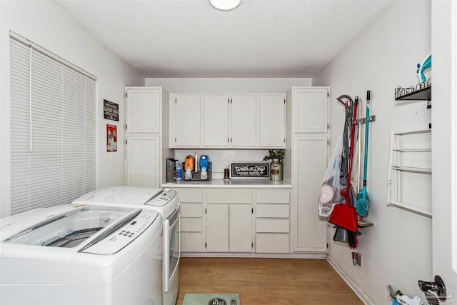 laundry room featuring light wood-type flooring, a textured ceiling, washing machine and dryer, and cabinets