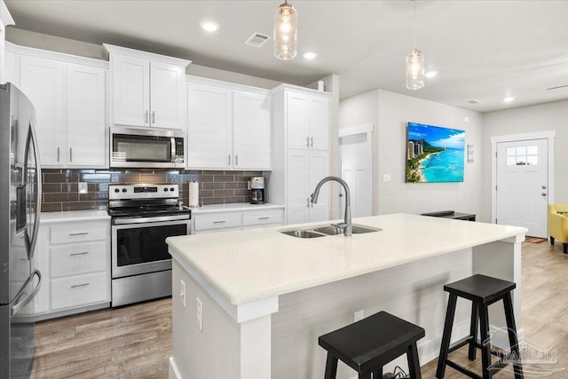 kitchen with a center island with sink, stainless steel appliances, white cabinets, and decorative light fixtures