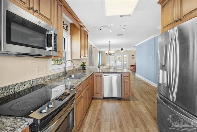 kitchen featuring light stone countertops, light wood-type flooring, kitchen peninsula, stainless steel appliances, and a chandelier