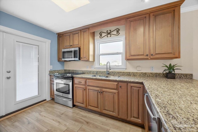 kitchen with sink, light stone countertops, ornamental molding, light hardwood / wood-style floors, and stainless steel appliances